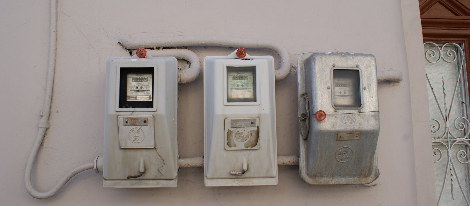 Trei contoare electrice de apartament montate pe peretele unei case, cu cabluri albe