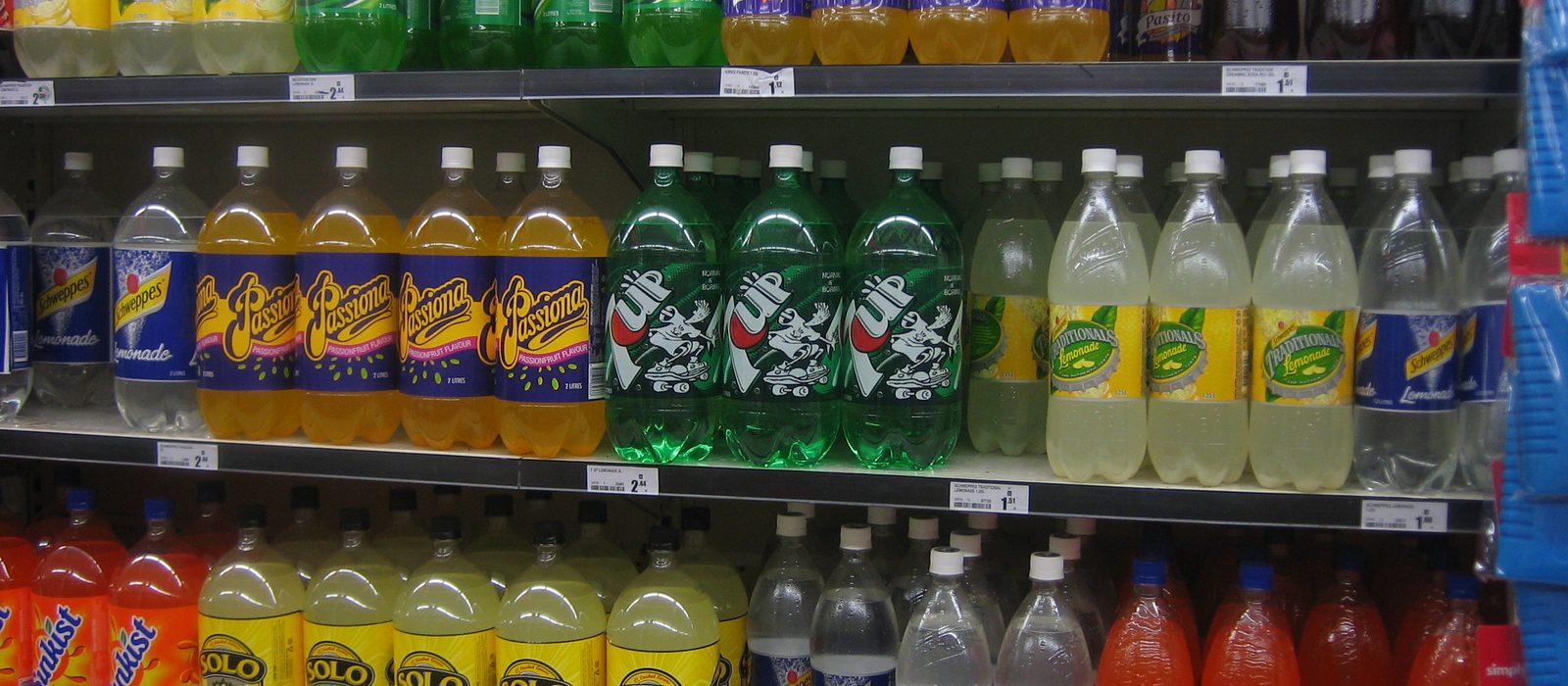 Rafturi de supermarket cu sticle de doi litri de limonade și băuturi carbogazoase, cu etichete de preț