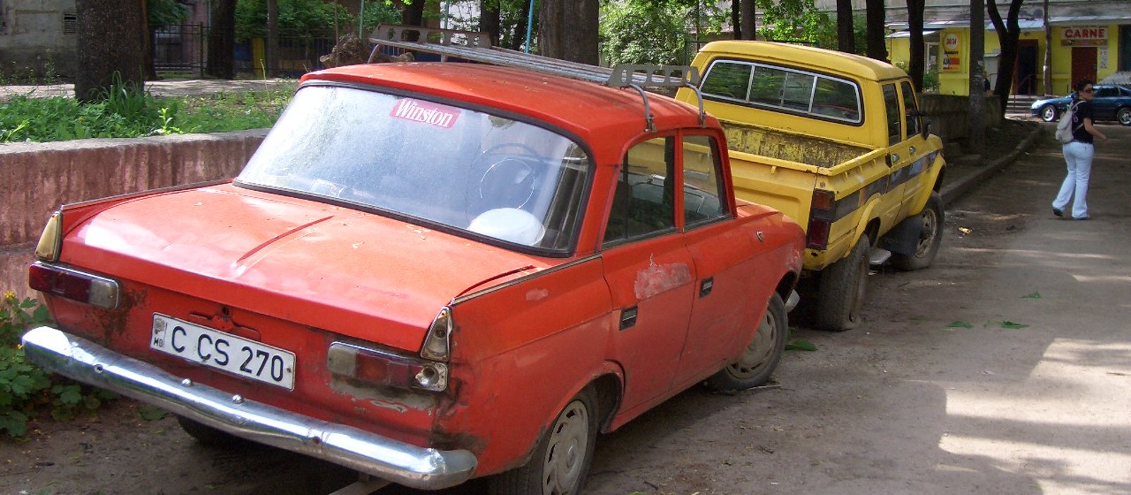 Un autoturism roșu vechi parcat lângă o camionetă galbenă pe o alee din Chișinău