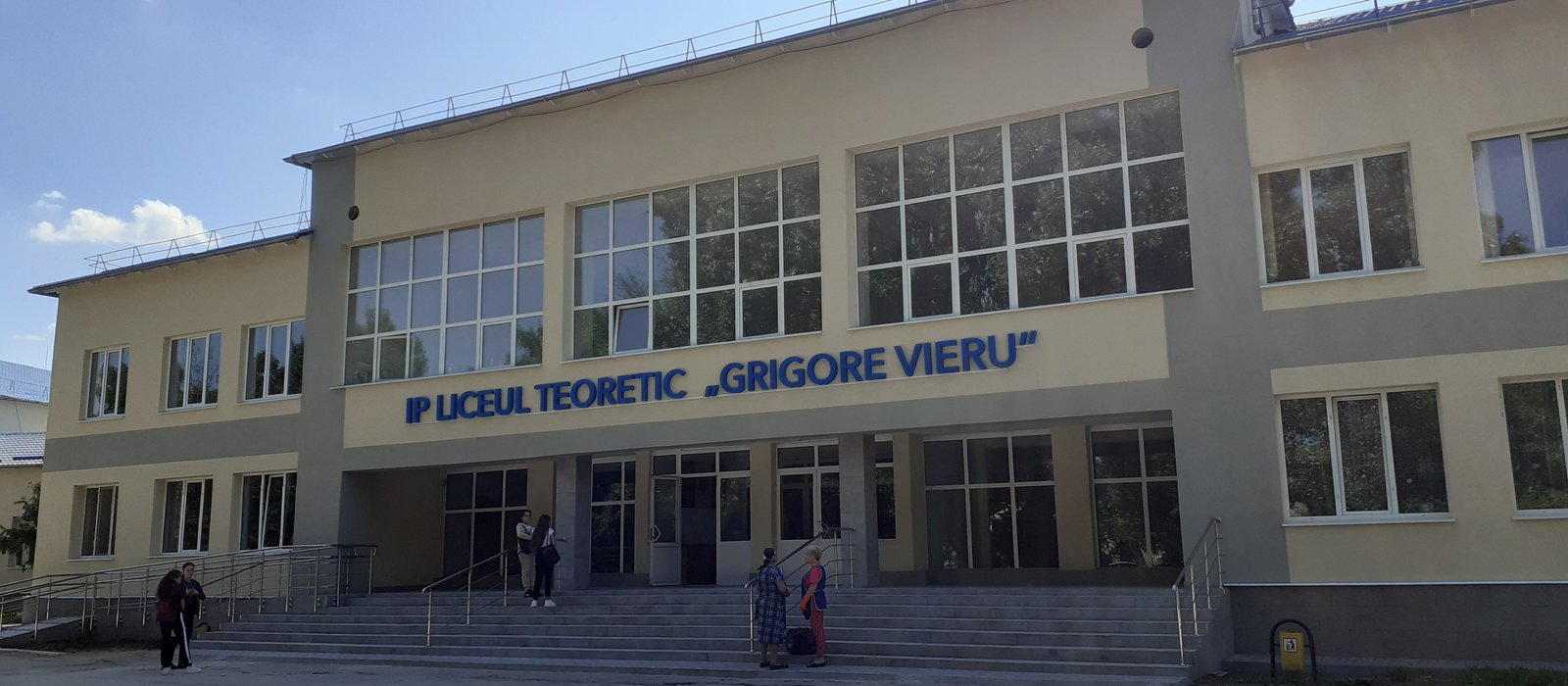 Fațada liceului teoretic Grigore Vieru din Băcioi, cu treptele de la intrare și câțiva oameni în față