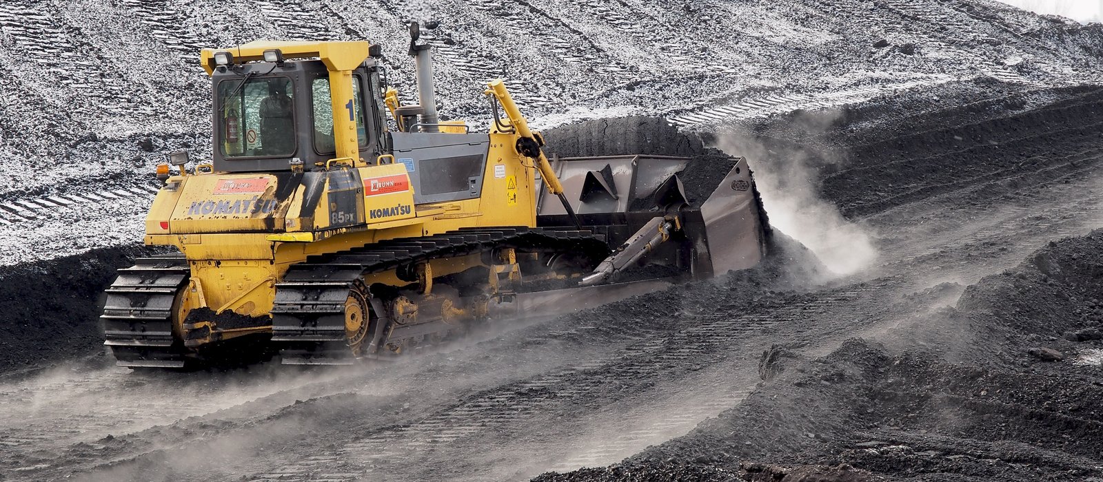 Un buldozer împinge un morman de cărbune pe platforma unei centrale electrice, iarna