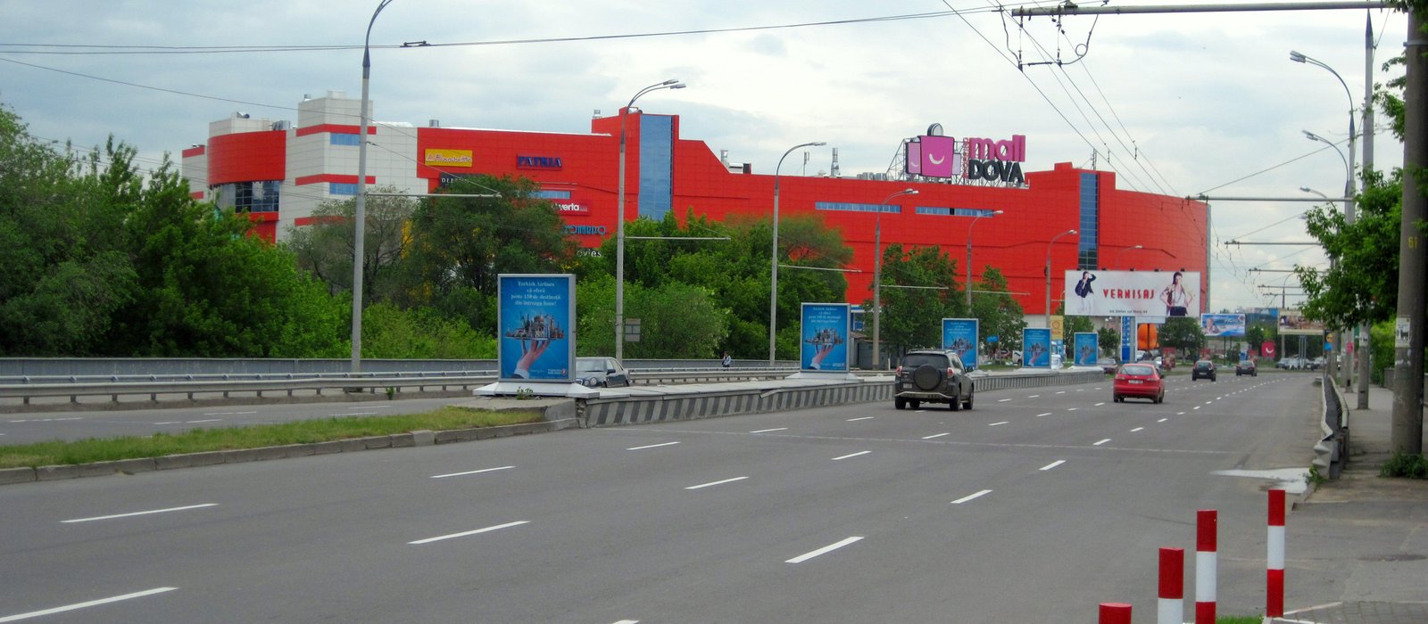 Bulevard cu mai multe benzi în Chișinău, cu clădirea roșie a centrului comercial MallDova în fundal