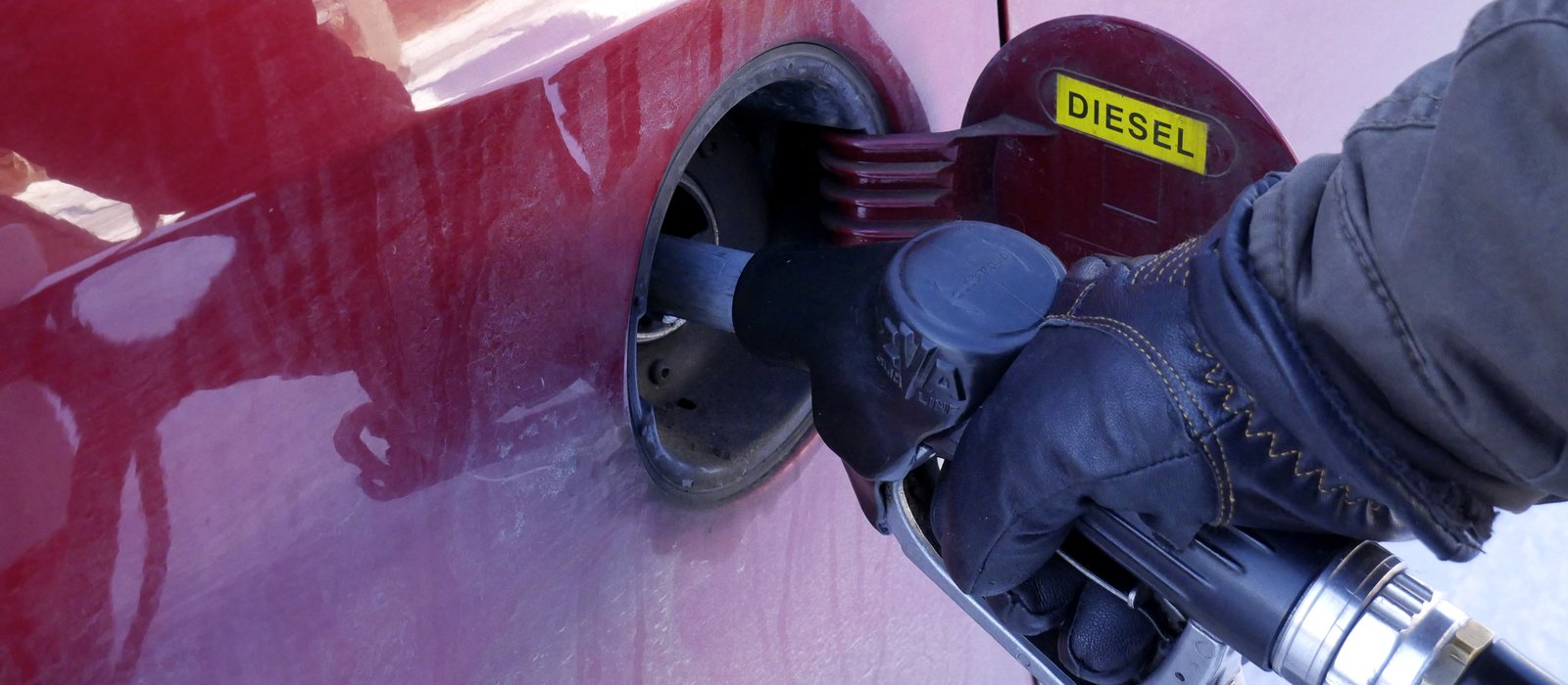 Mână în mănușă ține pistolul de alimentare introdus în rezervorul unei mașini roșii, cu autocolantul Diesel pe capac