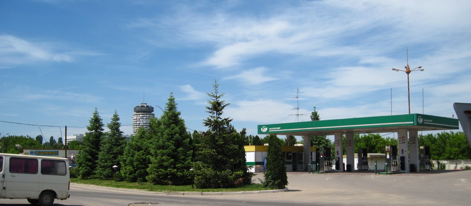 Stație de alimentare cu copertină verde la Chișinău, cu un microbuz alb în stânga și blocuri în fundal