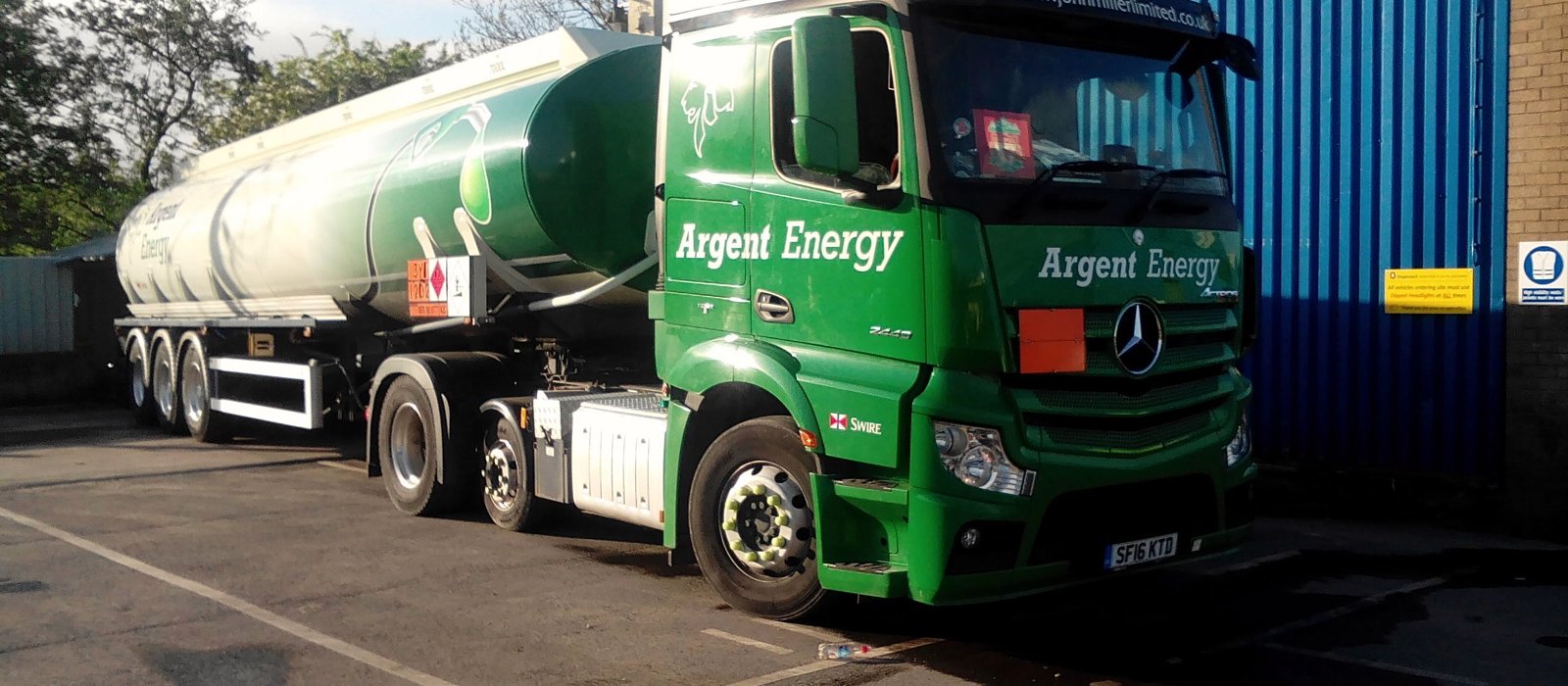 Autocisternă verde parcată lângă un depot, cu încărcătura de combustibil marcată cu panou portocaliu