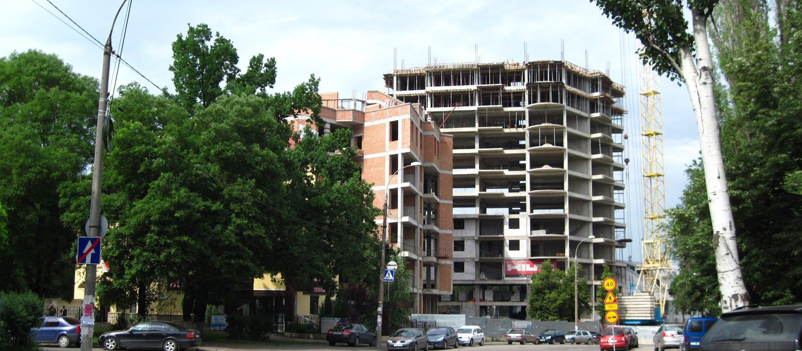 Bloc de locuințe cu structura din beton încă neterminată, lângă o macara galbenă, pe o stradă din Chișinău