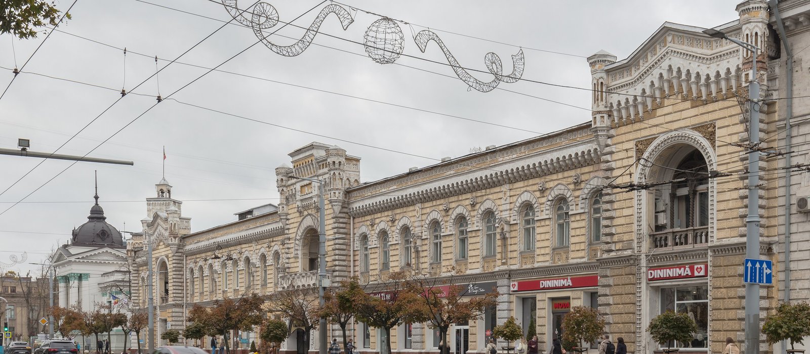 Fațada istorică a Primăriei Chișinău, pe o stradă din centrul capitalei, cu pietoni și vitrine la parter