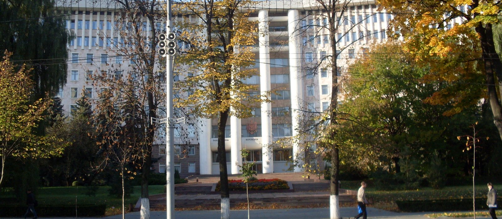 Clădirea Parlamentului Republicii Moldova din Chișinău, cu coloane albe, văzută printre copaci toamna