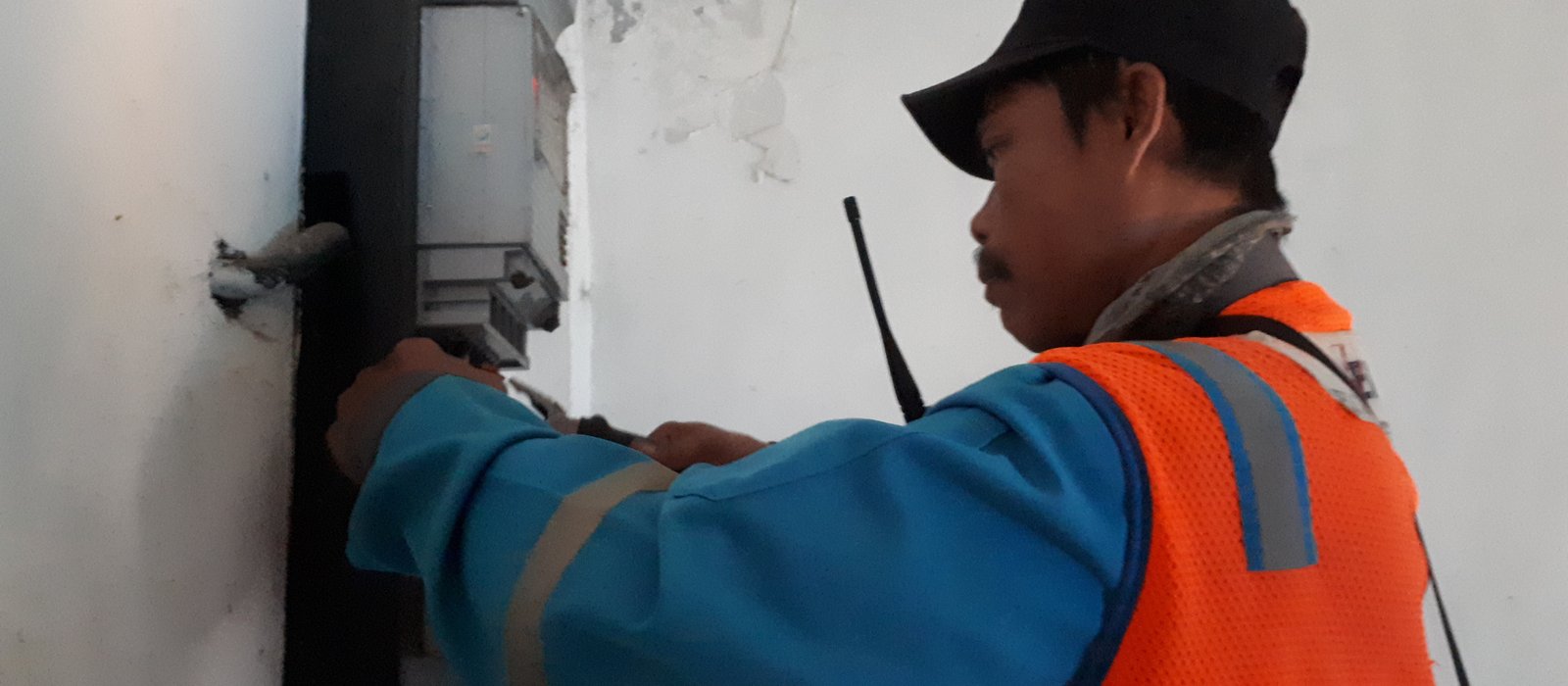 Un electrician în vestă reflectorizantă lucrează la un contor de electricitate montat pe un perete