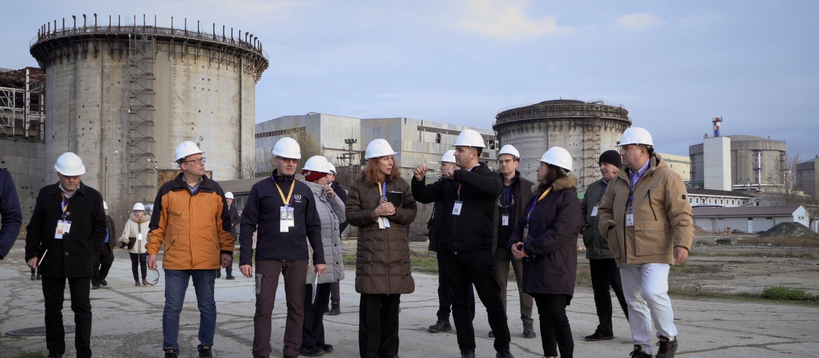 Un grup de inspectori în căști albe pe platforma centralei nucleare de la Cernavodă, cu clădirile reactoarelor în fundal