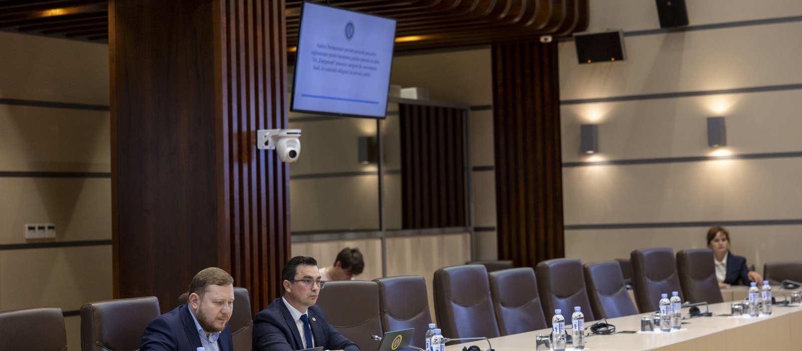 Audiere într-o sală a Parlamentului Republicii Moldova, cu doi oficiali la masă și un ecran care anunță subiectul despre Energocom