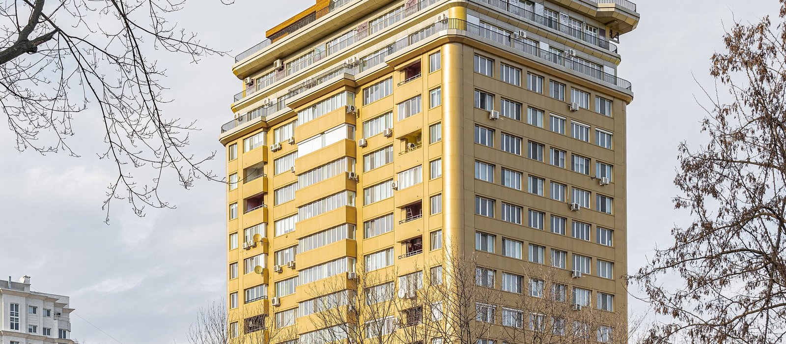 Bloc înalt cu fațadă aurie pe strada București din Chișinău, văzut printre crengi de toamnă