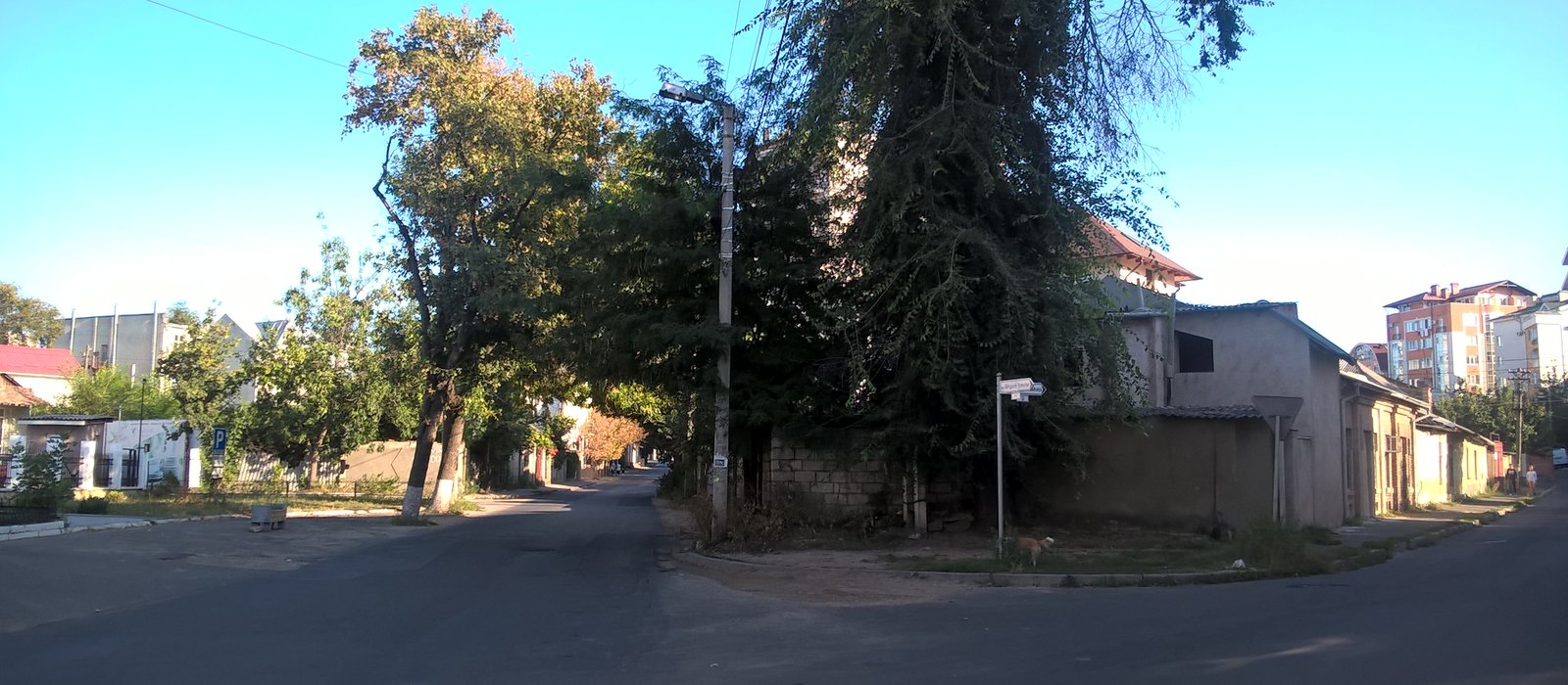 Intersecție de străzi liniștite din Chișinău, cu case joase, copaci și blocuri în fundal