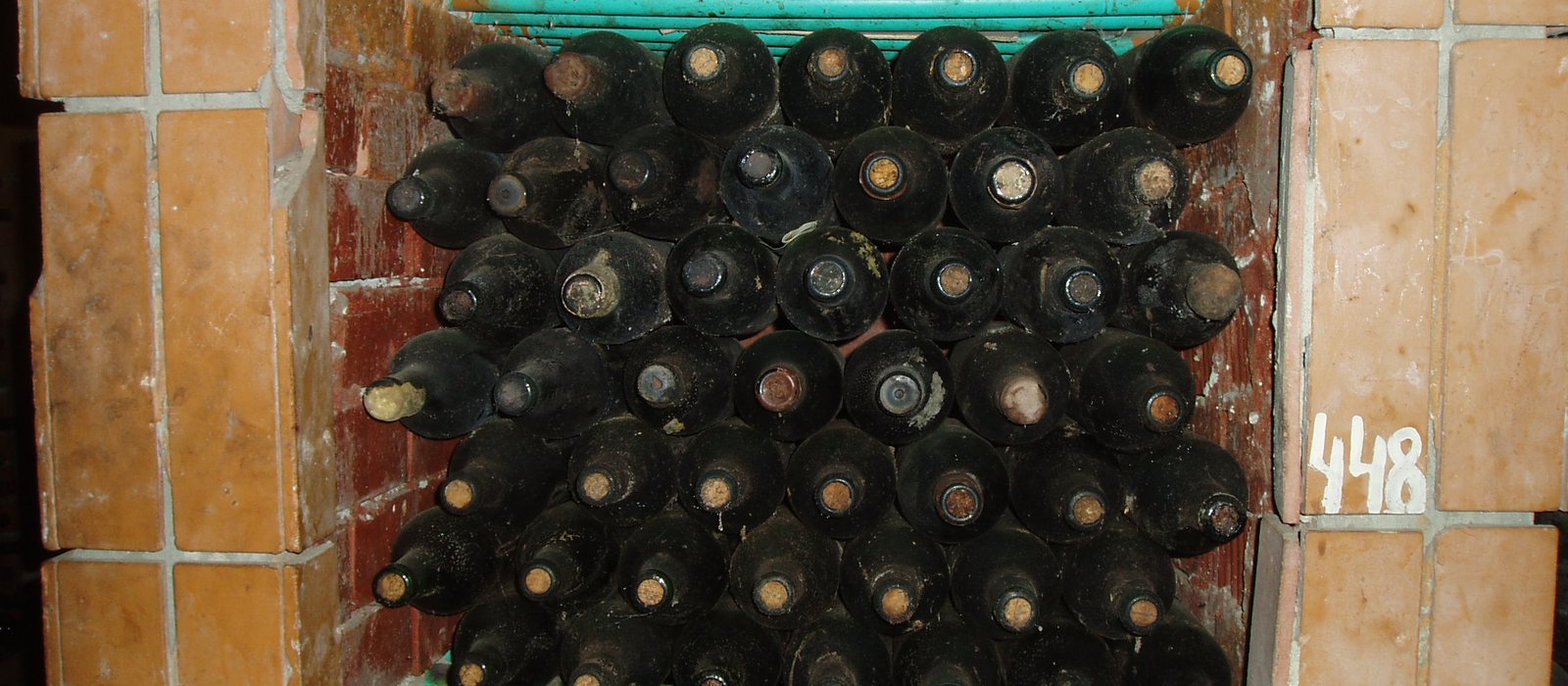 Sticle de vin prăfuite, stivuite pe rânduri într-o nișă de cărămidă din pivnițele vinăriei Cojușna, lângă Chișinău