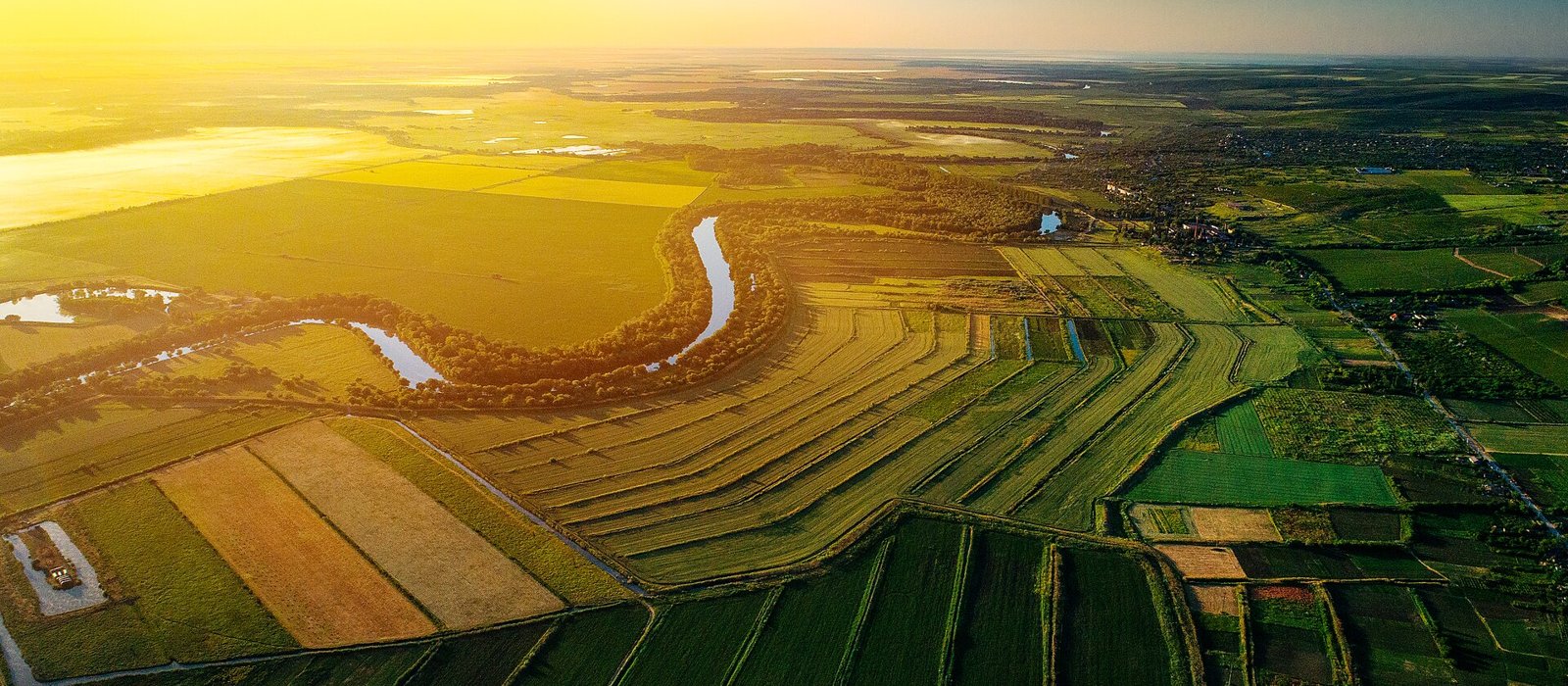 Vedere aeriană la apus asupra unor terenuri agricole și a unui râu cu meandre în Republica Moldova