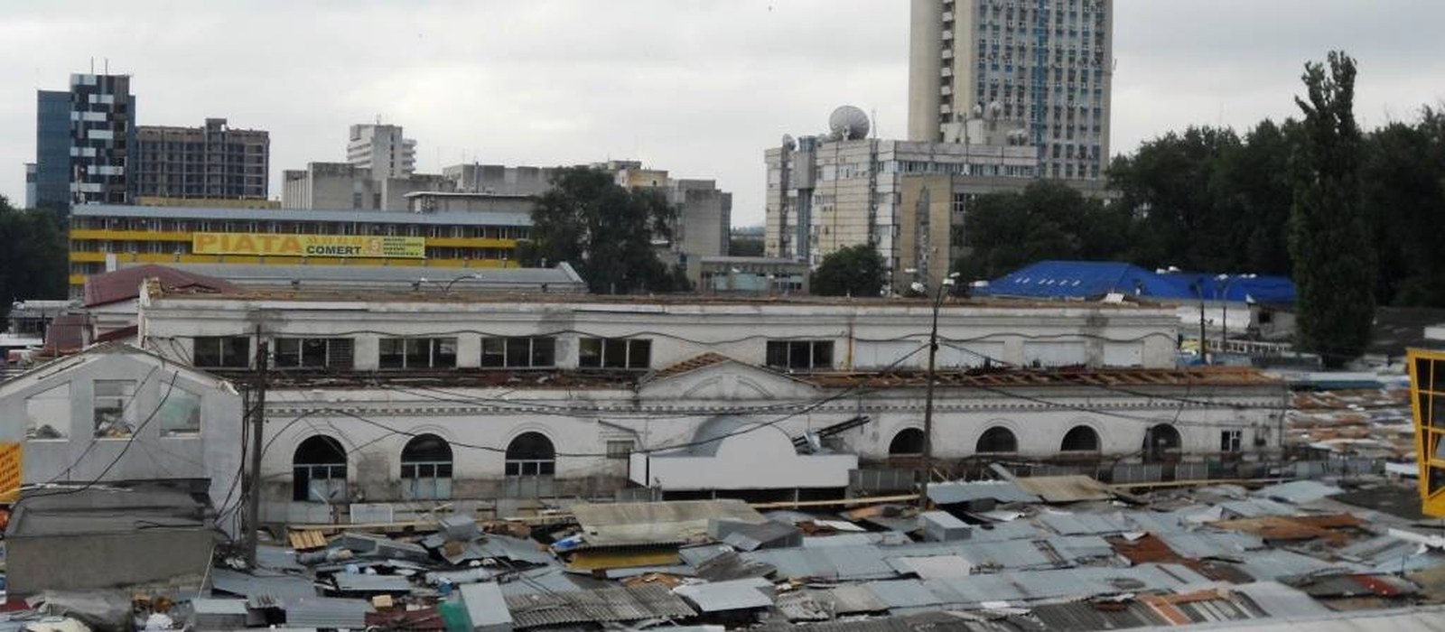 Hala veche a Pieței Centrale din Chișinău, cu acoperișurile tarabelor în față și blocuri în fundal