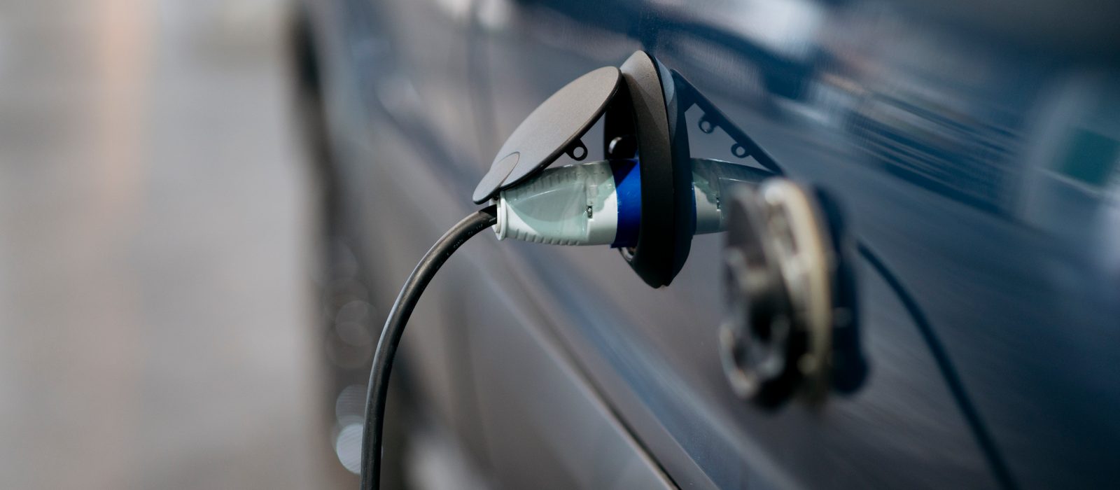 Ștecărul unui cablu de încărcare introdus în portul unei mașini electrice albastre