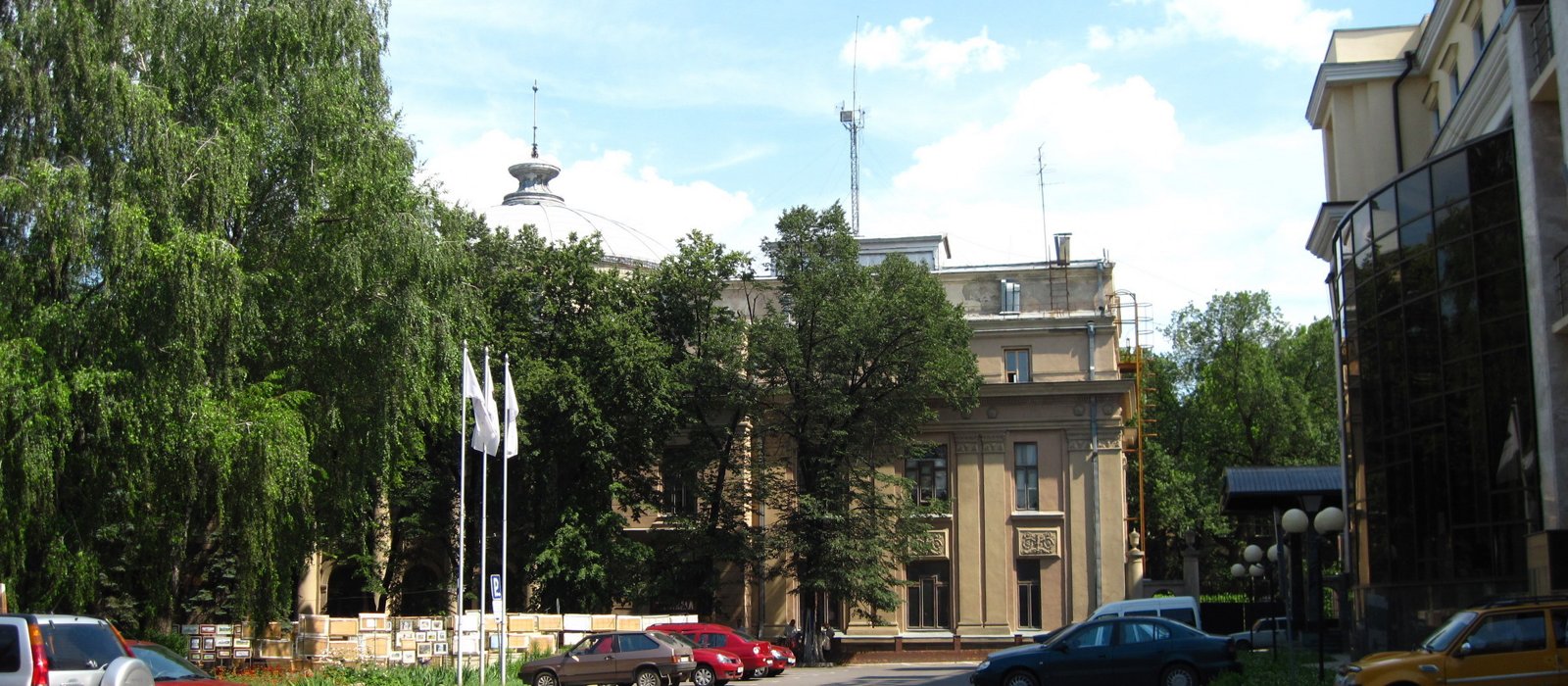 Mașini parcate pe o alee din centrul Chișinăului, lângă o clădire administrativă și copaci mari