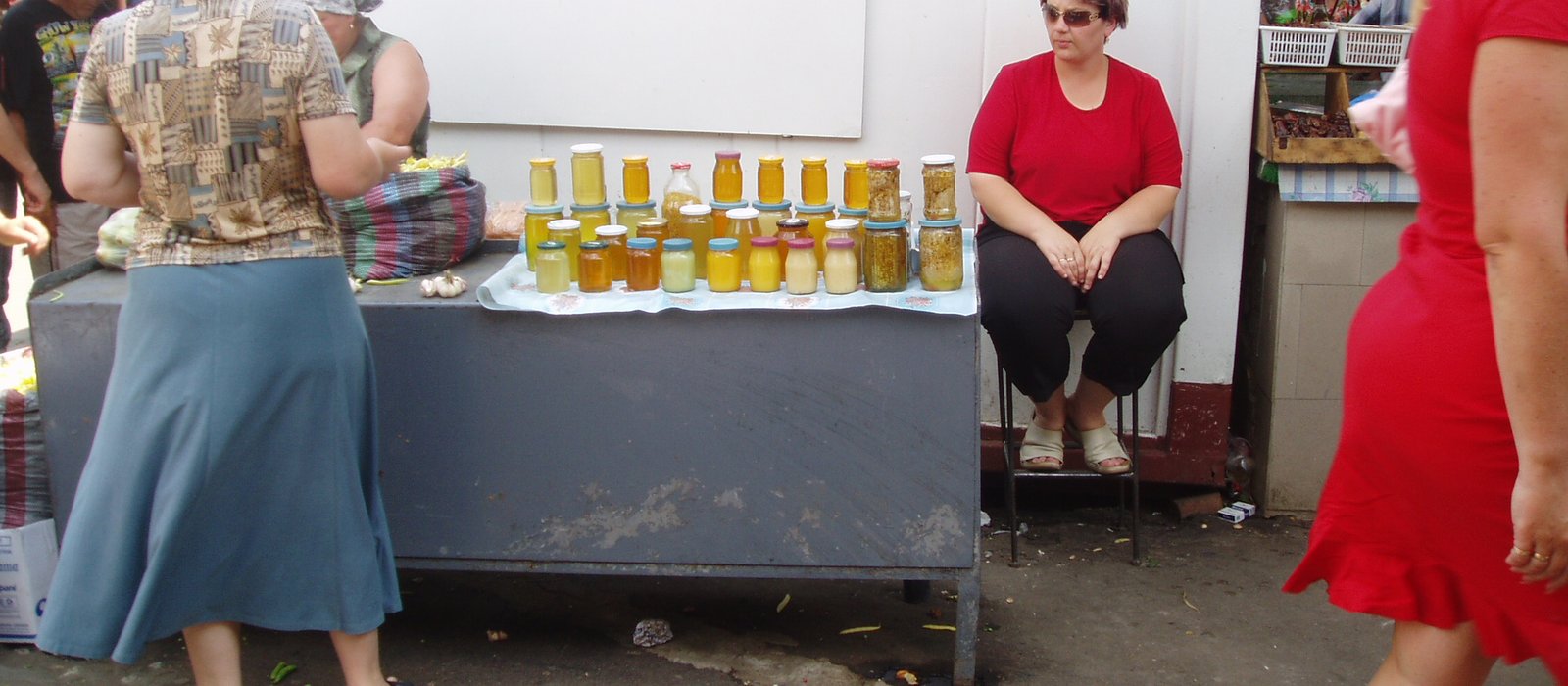 Un stand cu borcane de miere pe masa unei vânzătoare din Piața Centrală din Chișinău, cu cumpărători în față