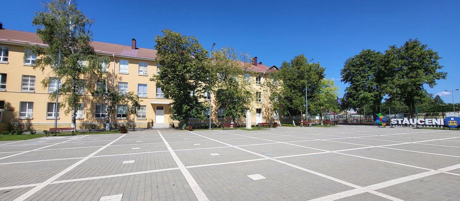 Clădirea galbenă a liceului și piața pavată din centrul orașului Stăuceni, lângă Chișinău, sub cerul senin