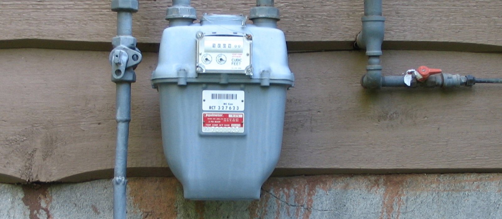 Un contor de gaz montat pe un perete de cărămidă, cu țeavă galbenă de racordare