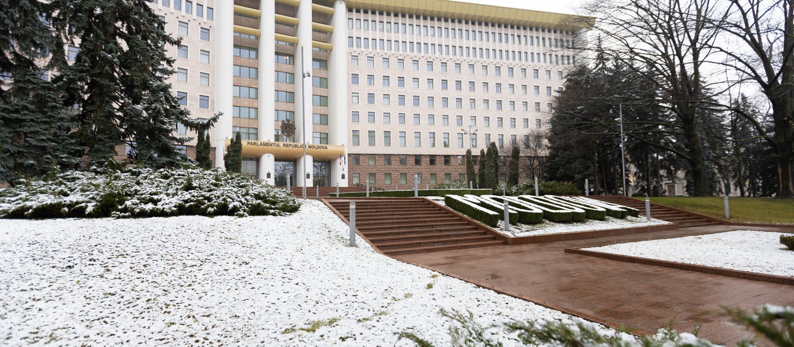 Fațada clădirii Parlamentului Republicii Moldova la Chișinău, cu treptele de la intrare și gazonul acoperit de zăpadă