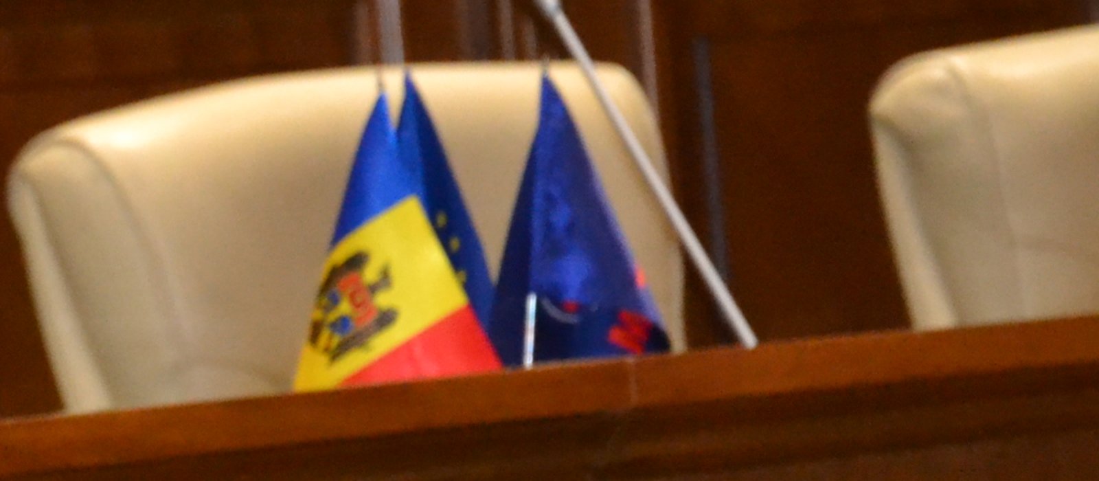 Steagurile Republicii Moldova și al Uniunii Europene pe un pupitru din sala de plen a Parlamentului, între scaune tapițate