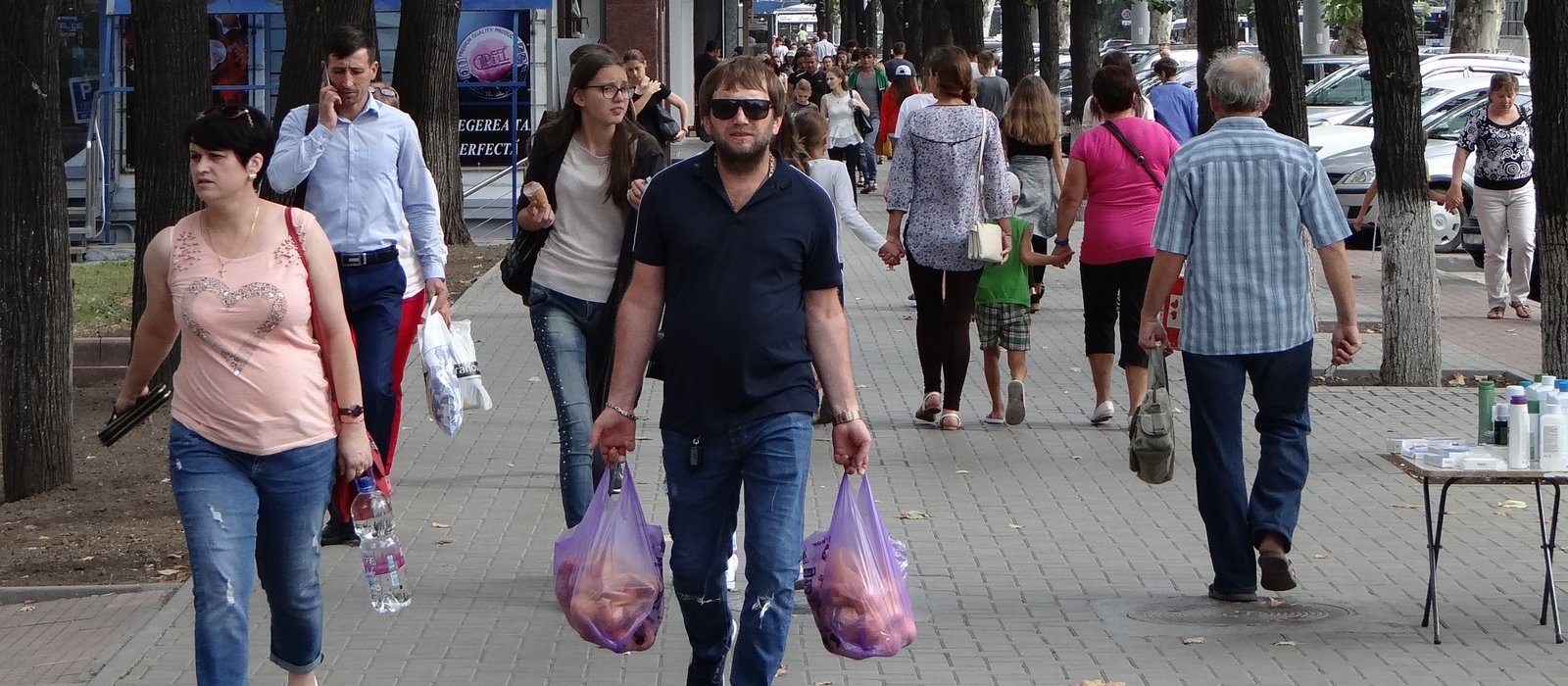 Trecători cu pungi de cumpărături pe un bulevard umbrit din Chișinău, între ei un bărbat în vârstă