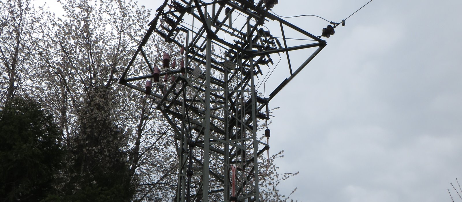 Stâlp terminal al unei linii electrice aeriene de medie tensiune, cu transformator, printre copaci înfloriți, lângă Dietershausen, în Germania