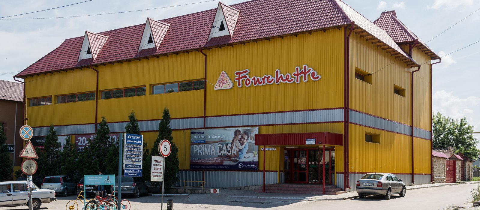 Clădire galbenă cu acoperiș roșu a unui supermarket din Edineț, cu parcare în față