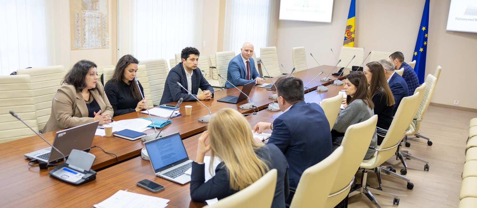 Ședință la comisia economică a Parlamentului Republicii Moldova, cu steagurile Moldovei și ale Uniunii Europene în fundal