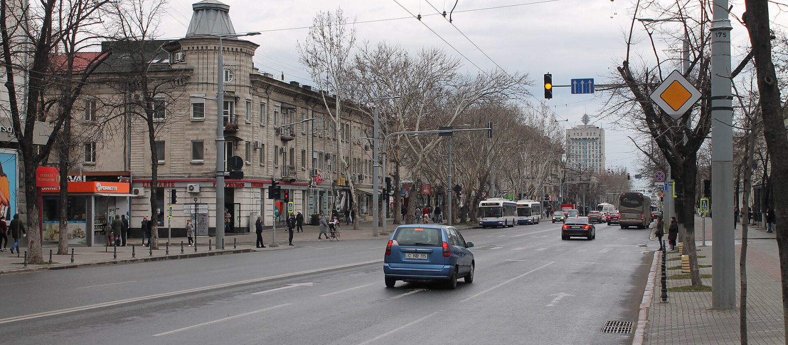 Un autoturism albastru și un autobuz pe bulevardul Ștefan cel Mare din Chișinău, cu copaci fără frunze pe margini