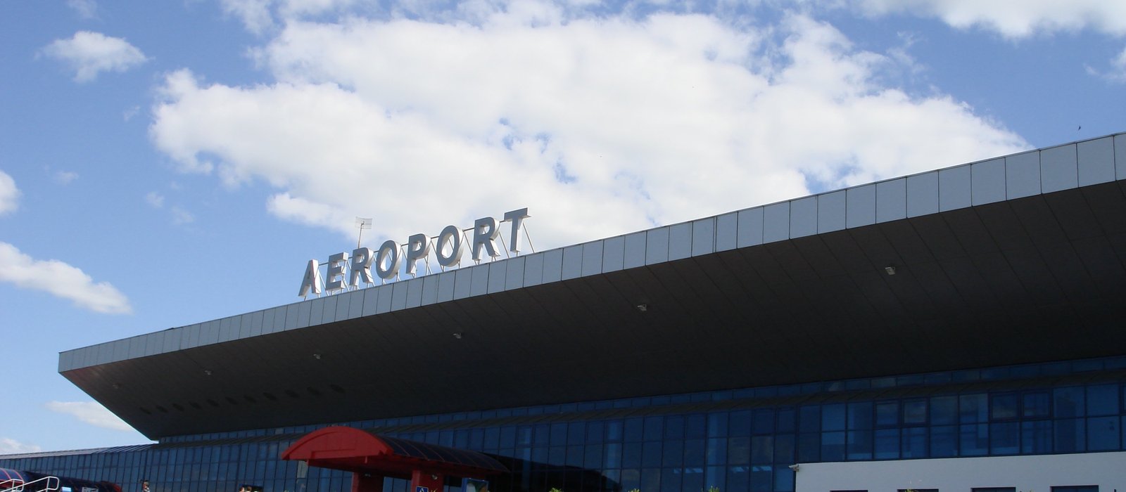 Fațada terminalului Aeroportului Internațional Chișinău, cu litere metalice AEROPORT pe acoperișul în consolă și cer cu nori