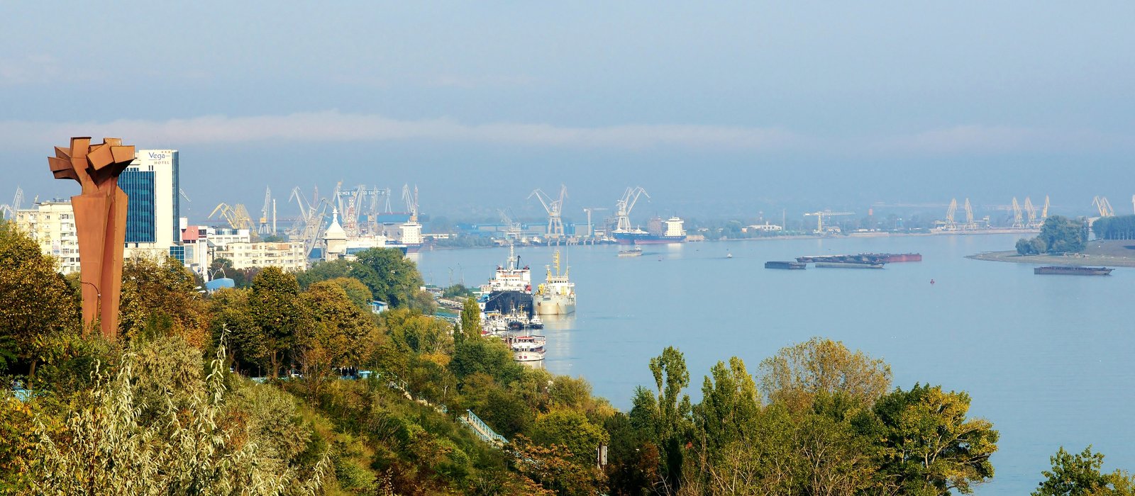 Macarale și nave în portul Galați, pe Dunăre, văzute de pe mal, cu dealul împădurit în prim-plan