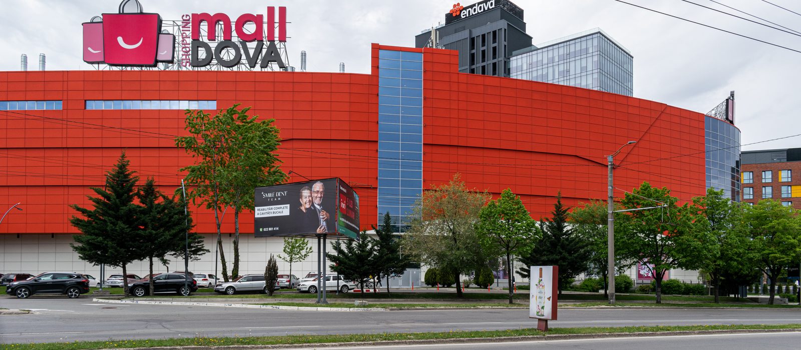 Fațada roșie a centrului comercial MallDova din Chișinău, cu turnul Endava în spate, într-o zi înnorată