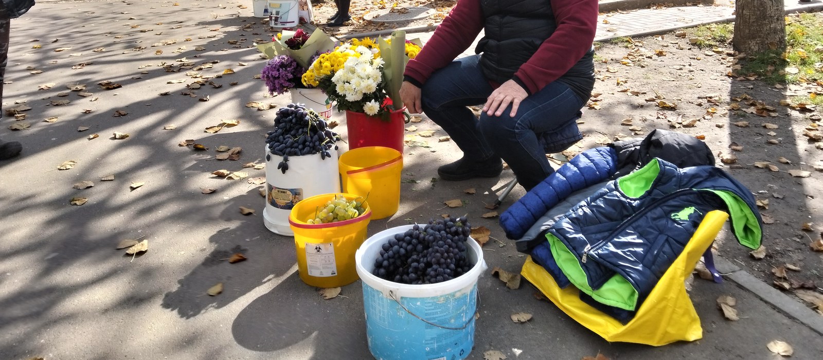 Struguri și crizanteme vândute în găleți pe un trotuar din Chișinău, într-o zi de toamnă