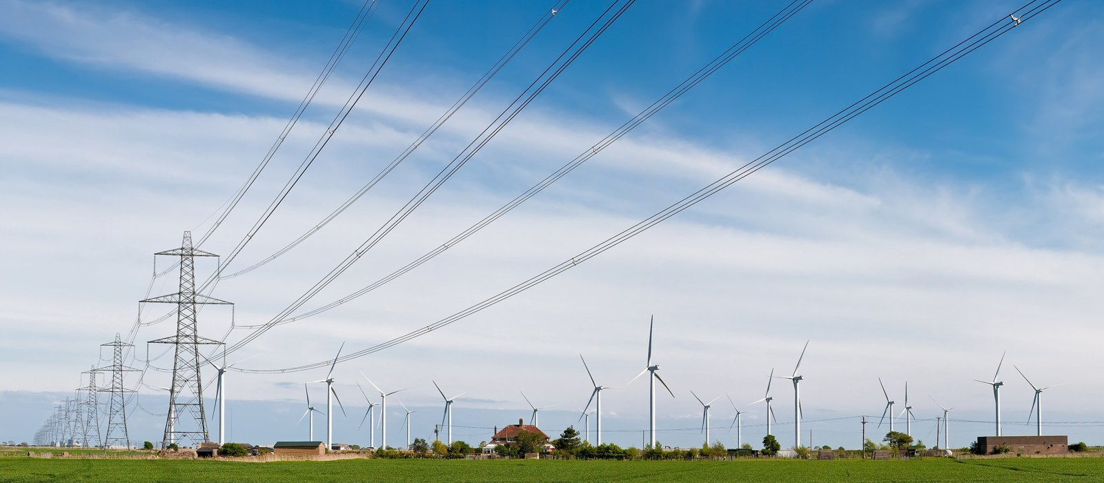 Turbine eoliene și linii electrice pe un câmp agricol, sub un cer cu nori ușori