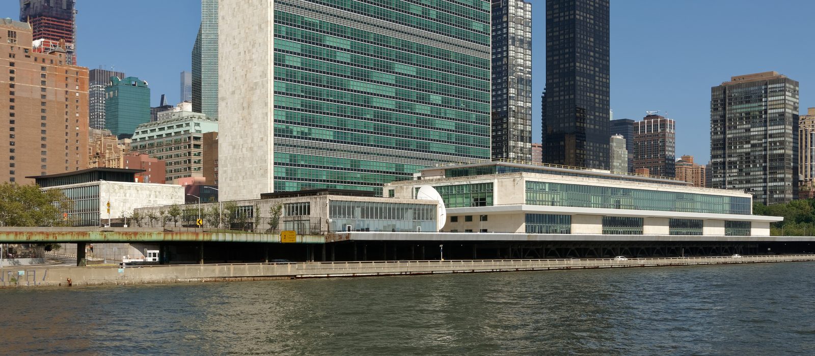 Clădirea Secretariatului ONU, un turn cu fațade de sticlă verzuie, și sala Adunării Generale pe malul râului East, New York