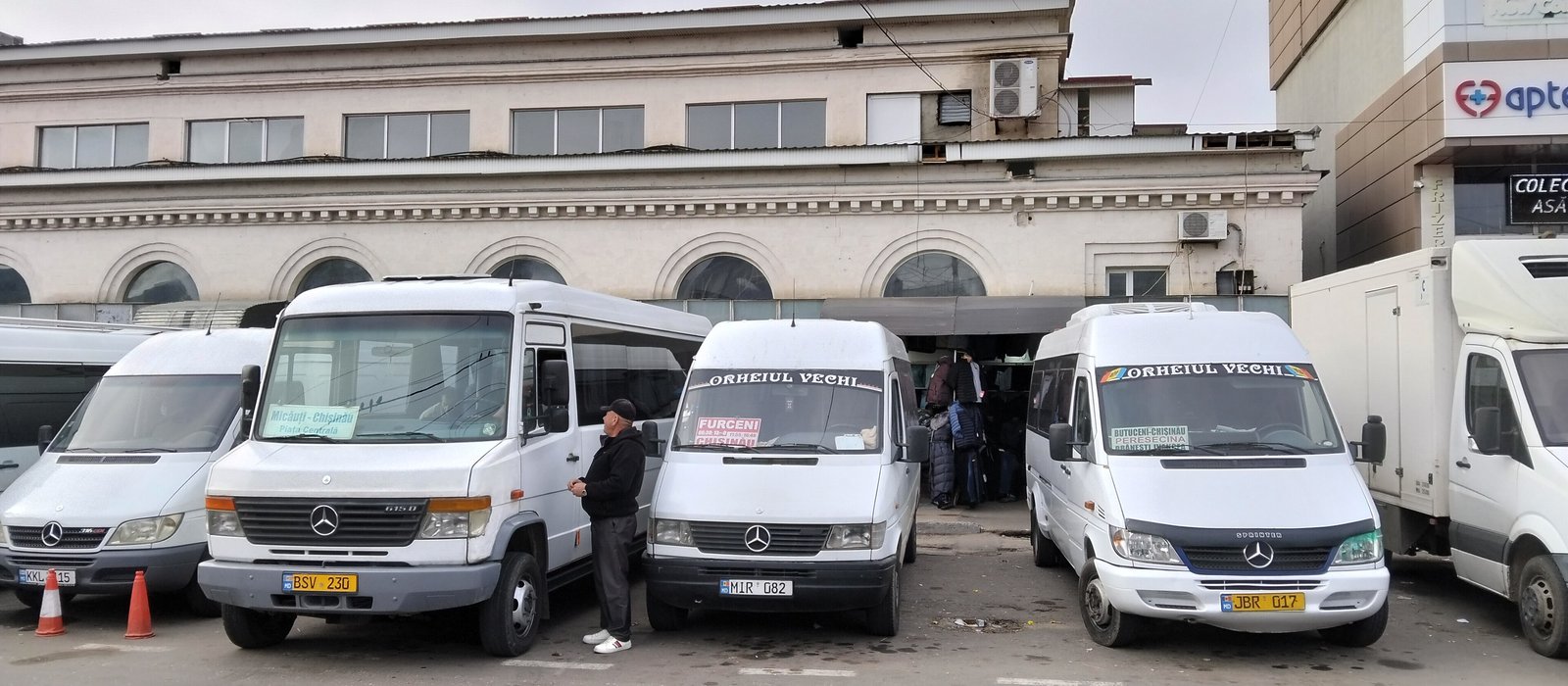Microbuze albe de pe rutele interurbane parcate în fața clădirii Gării Centrale din Chișinău, cu pasageri la intrare