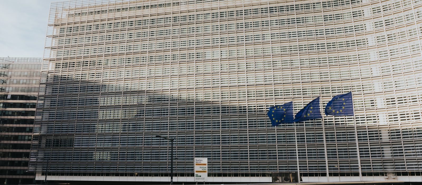 Clădirea Berlaymont din Bruxelles, sediul Comisiei Europene, cu trei drapele ale Uniunii Europene fluturând în fața fațadei
