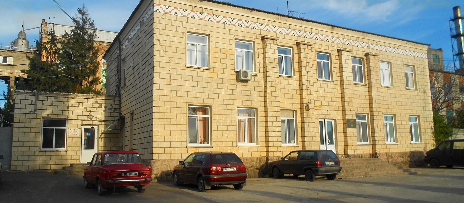 Clădirea administrativă din cărămidă galbenă a fabricii de zahăr din Fălești, cu mașini parcate în față și coșuri industriale în spate